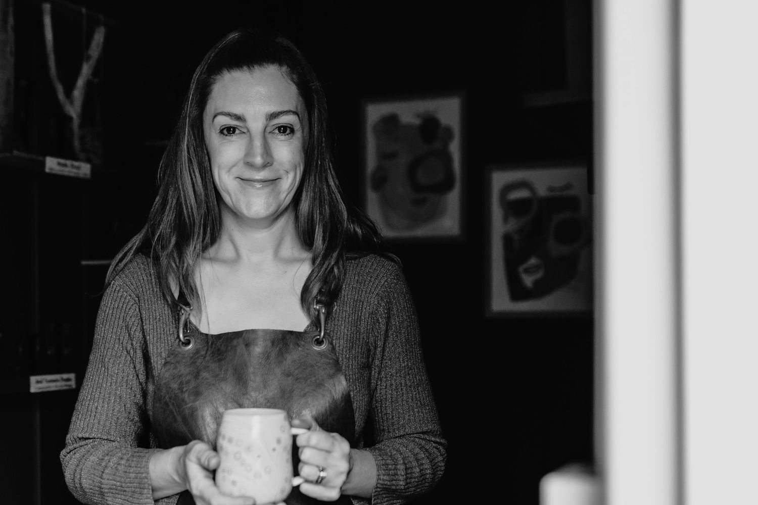 Black and white portrait of smiling woman holding white mug in cozy indoor setting.