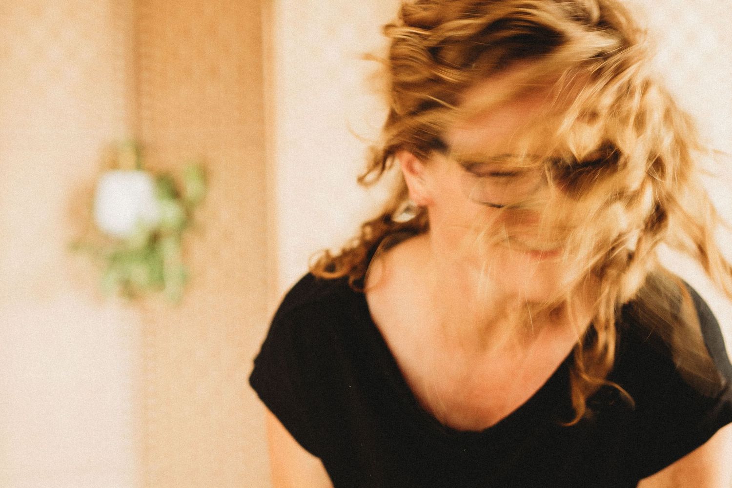 A blurred artistic portrait of a woman with braided hair tossing her head indoors.