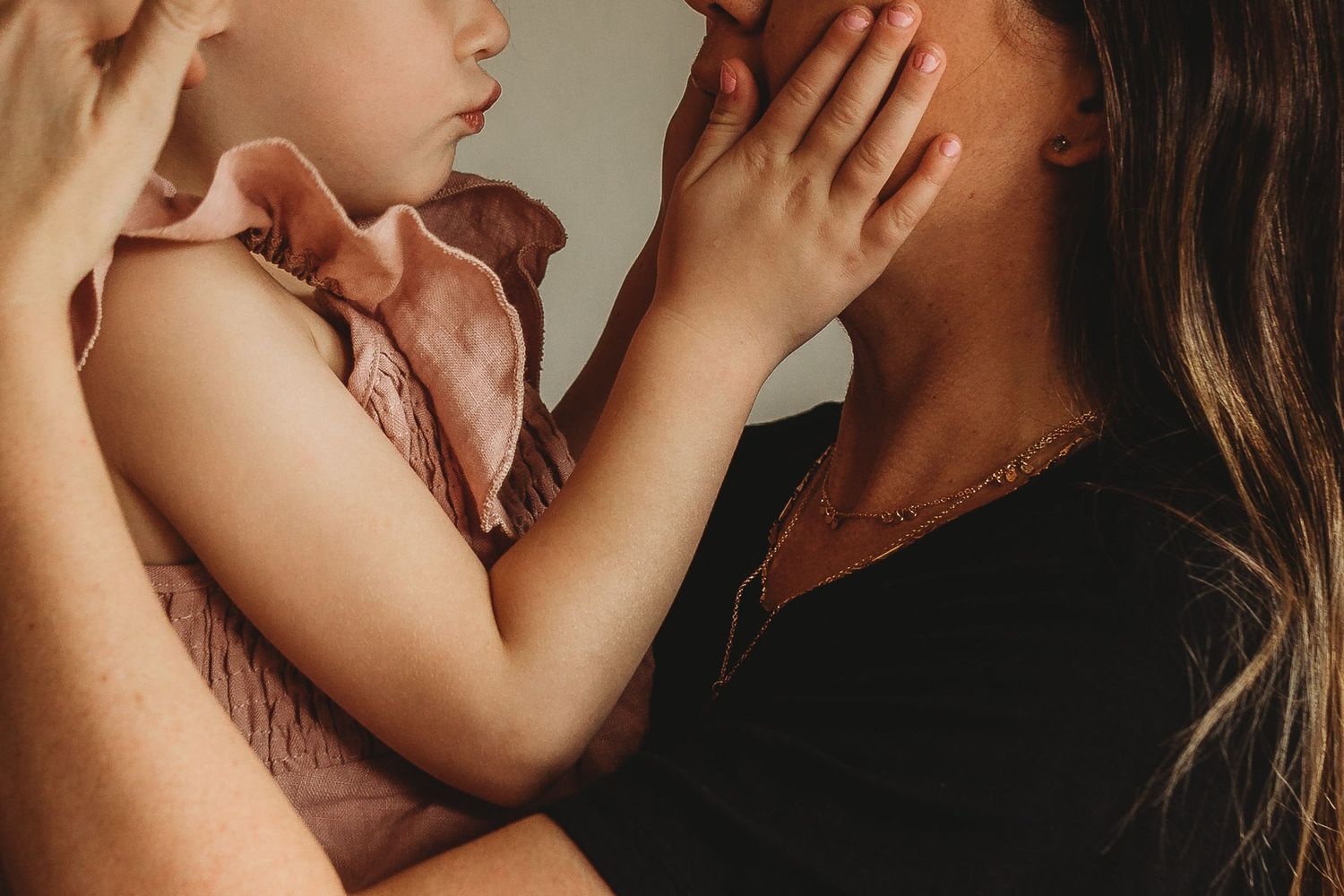 A mother tenderly holds her young daughter in a pink ruffled outfit close to her face.