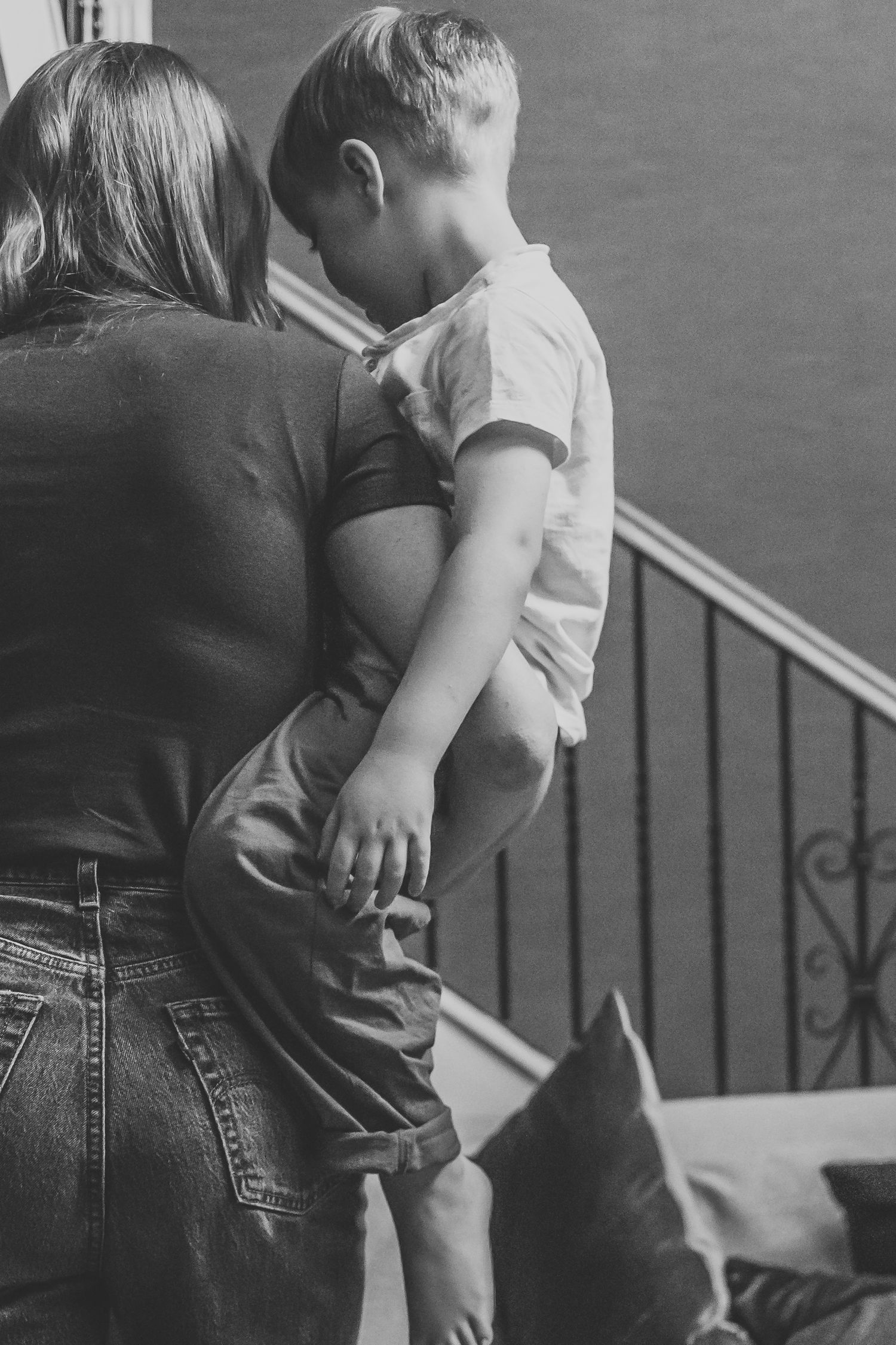 Black and white photo of a mother holding her young son near a staircase railing.