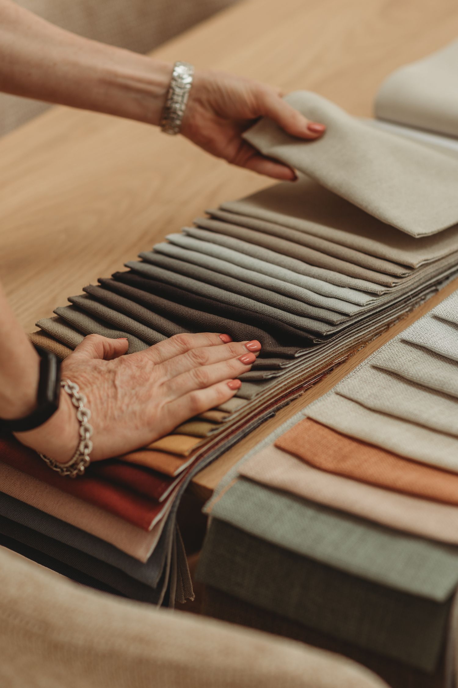 Interior designer hands browsing a collection of neutral linen fabric swatches in earthy tones on a wooden surface.