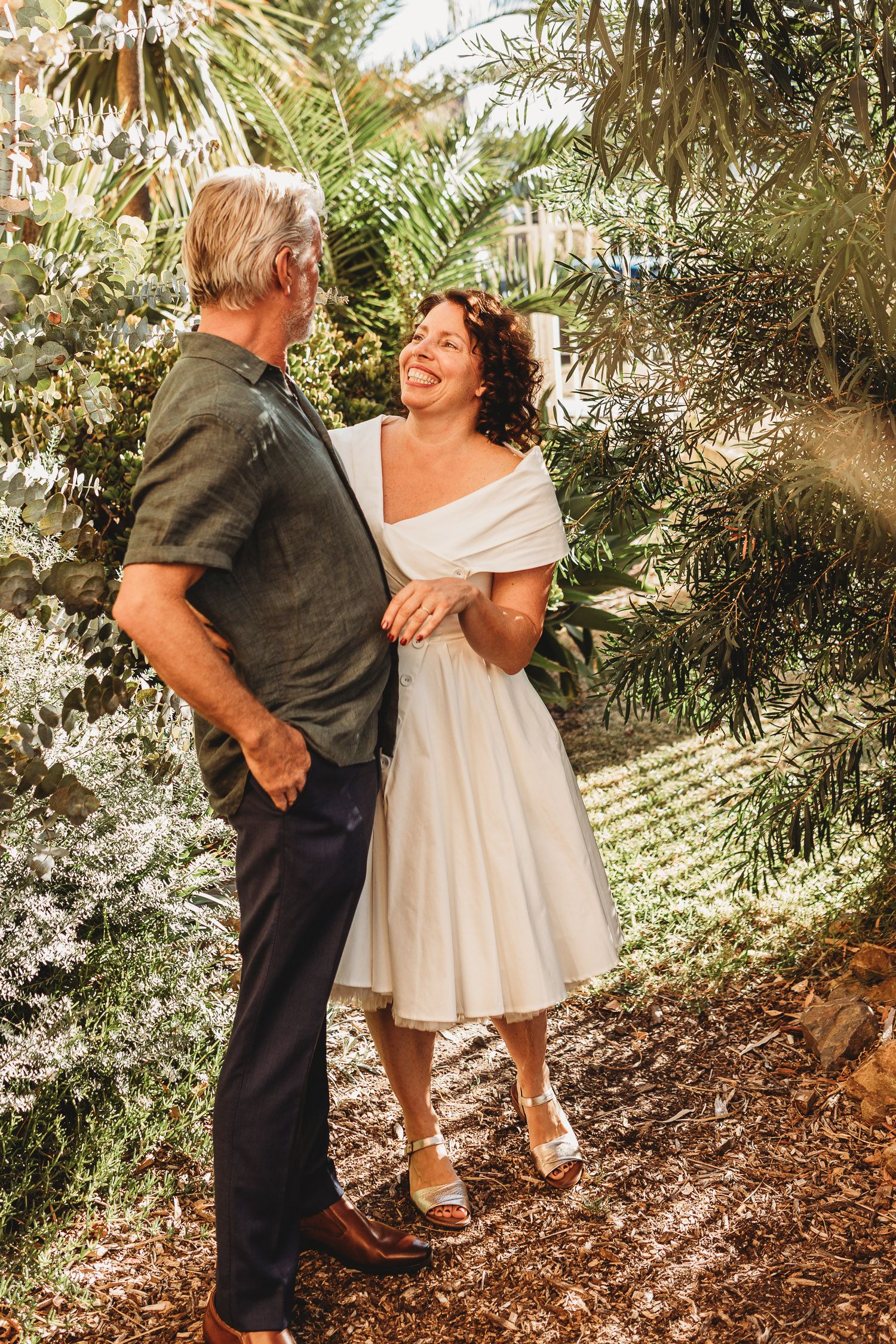 Couple sharing a joyful moment outdoors surrounded by lush tropical greenery on their wedding day.