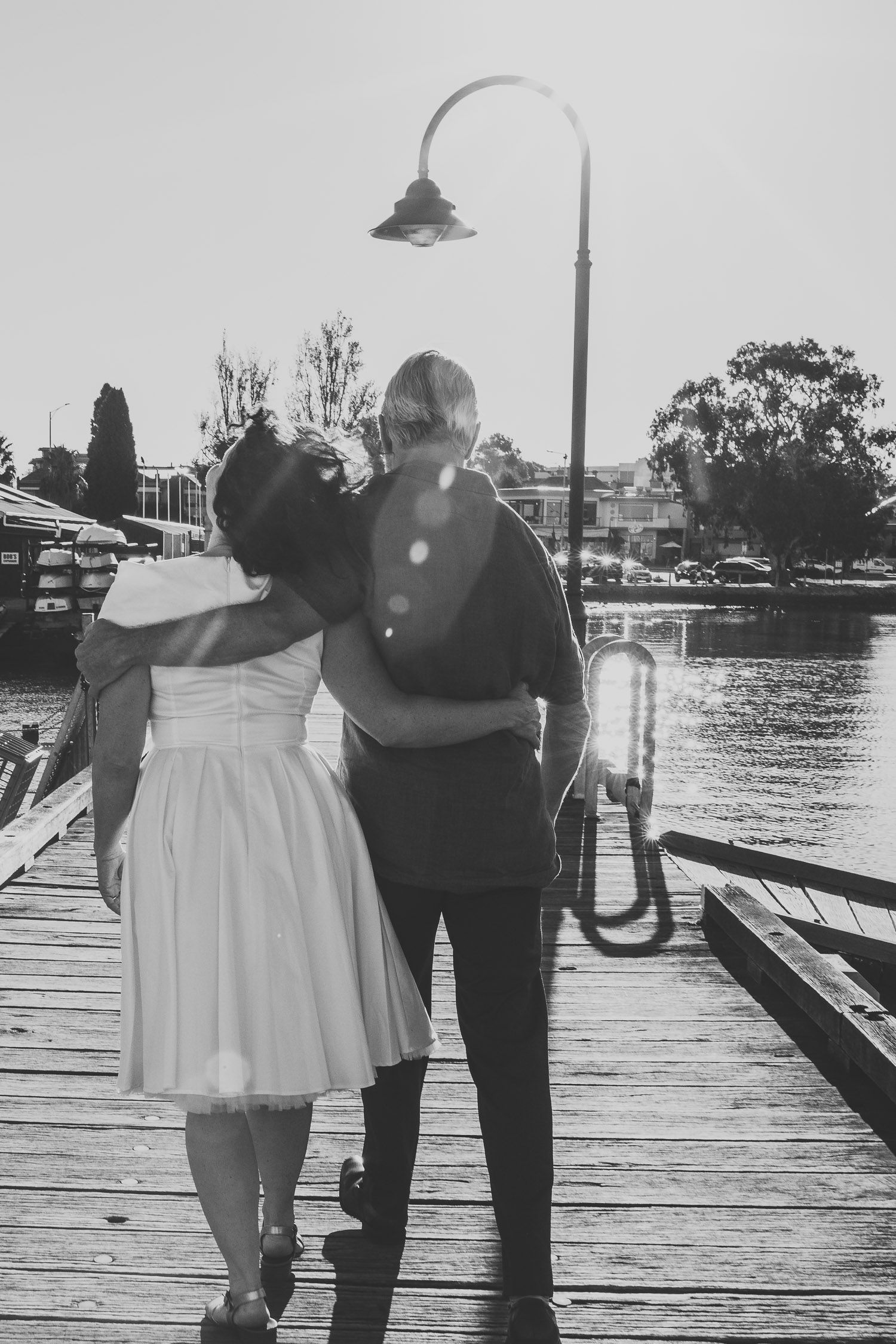 Bride and groom walking arm in arm along a marina pier in a romantic black and white wedding photo.