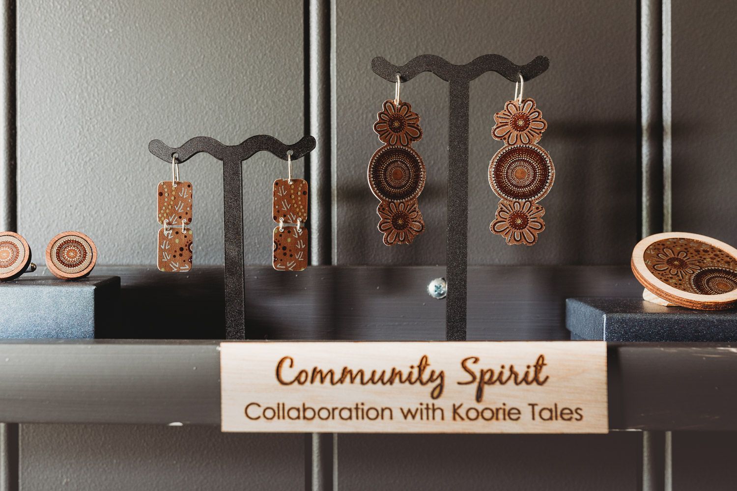 Wooden laser-cut earrings displayed on stand with Community Spirit Koorie Tales collaboration sign.