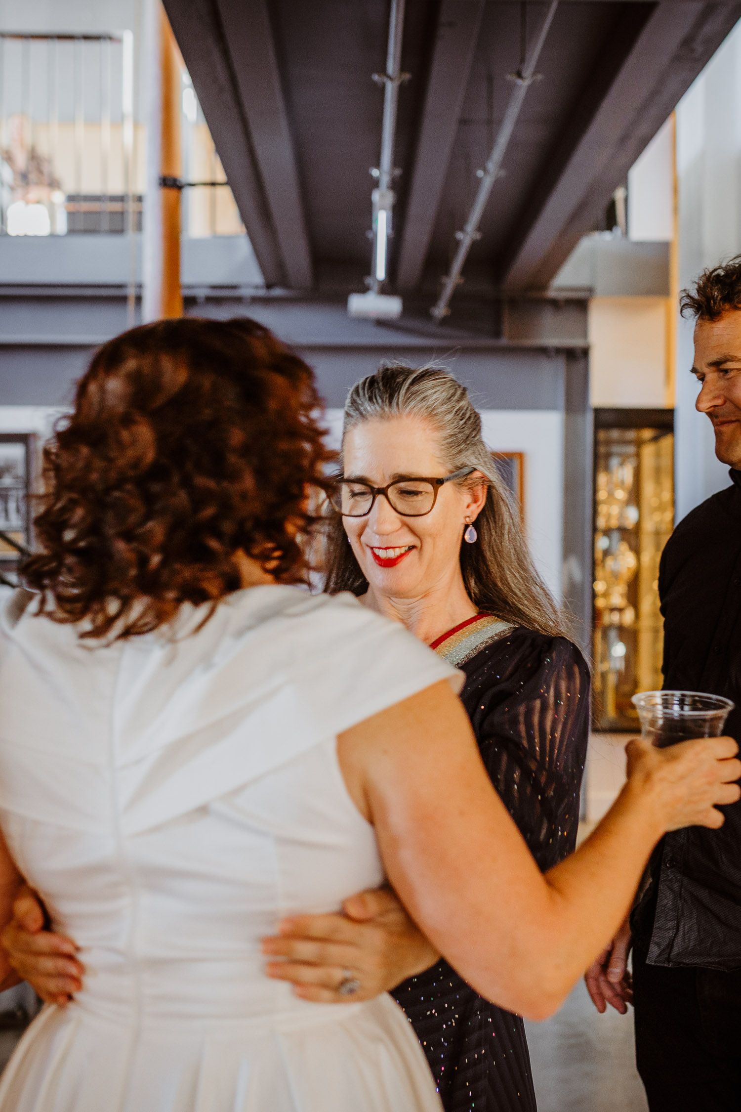 Wedding guest with gray hair and glasses smiling warmly at the bride in a white dress.