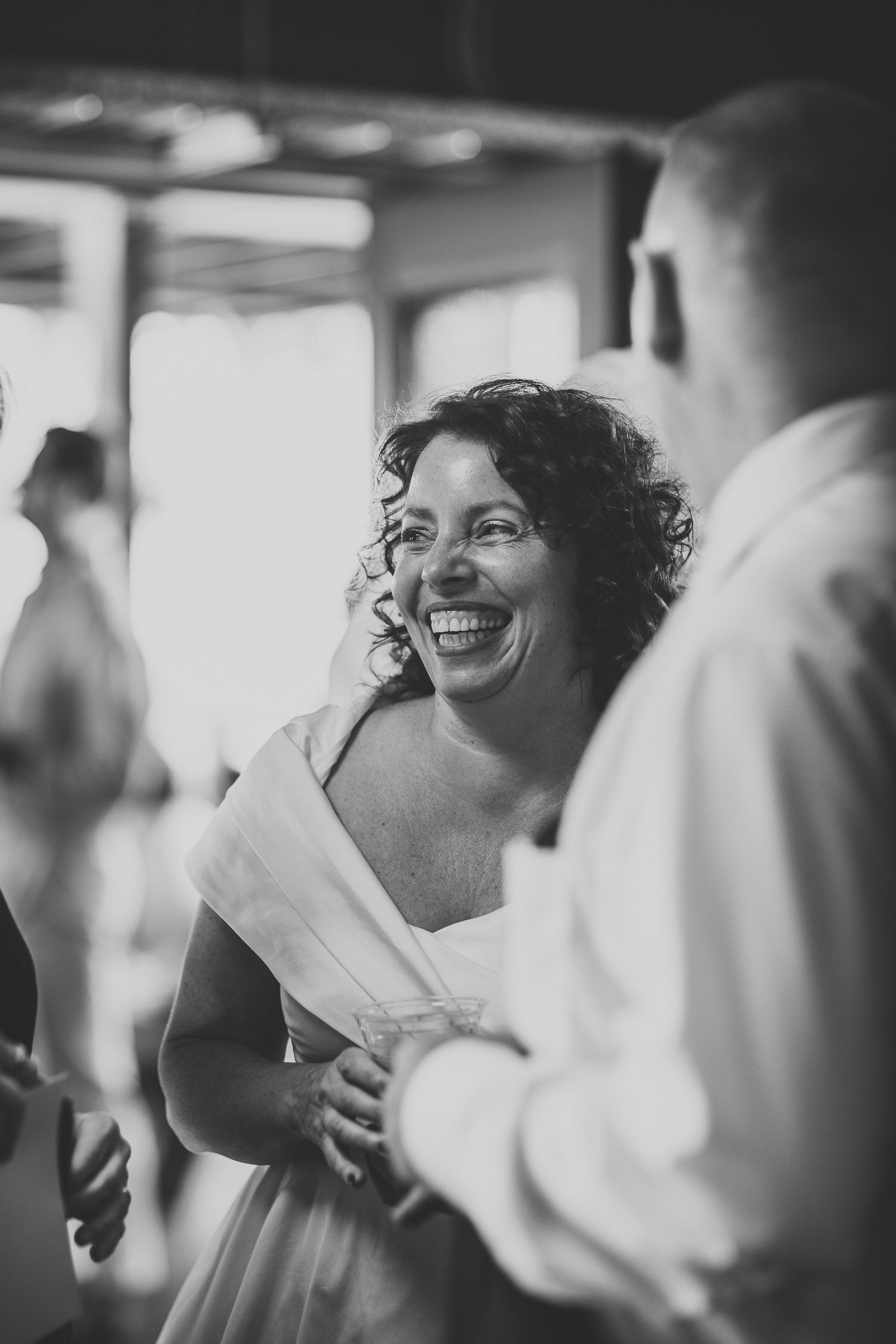 Black and white photo of a bride in a white dress laughing joyfully during her wedding reception.