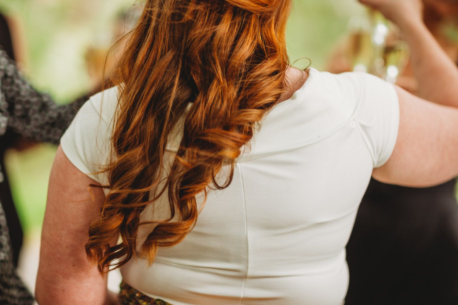 Close-up of a bride with long auburn curly hair wearing a white short sleeve wedding dress.