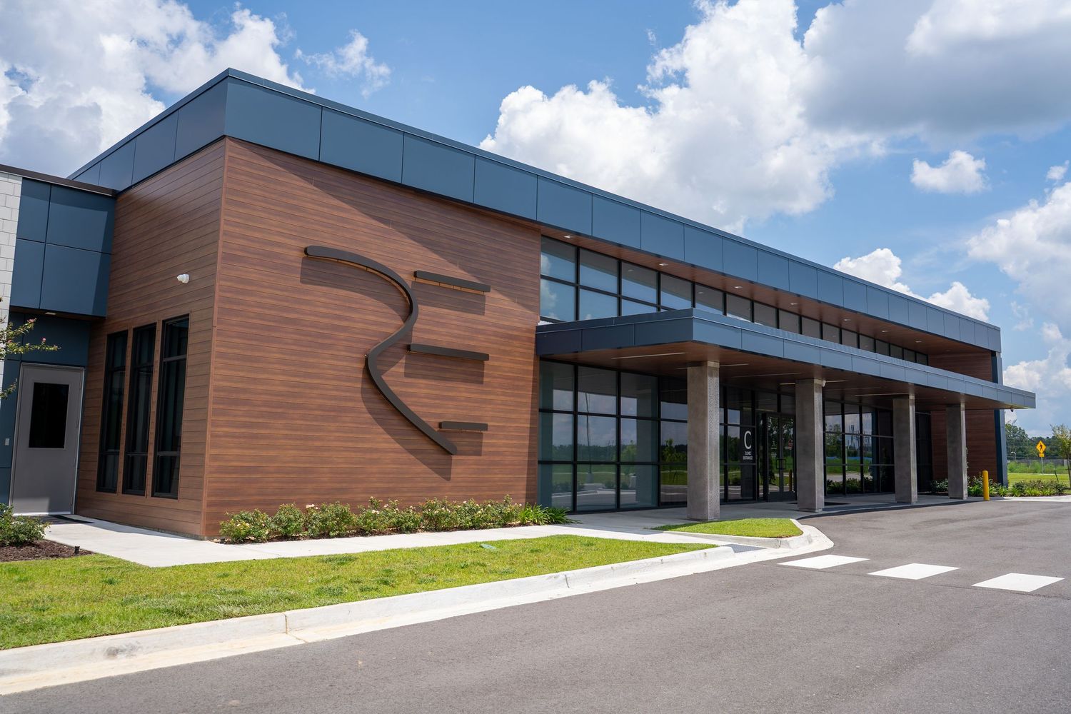Modern commercial building with brown brick facade, large windows, and RE logo signage under a partly cloudy sky.