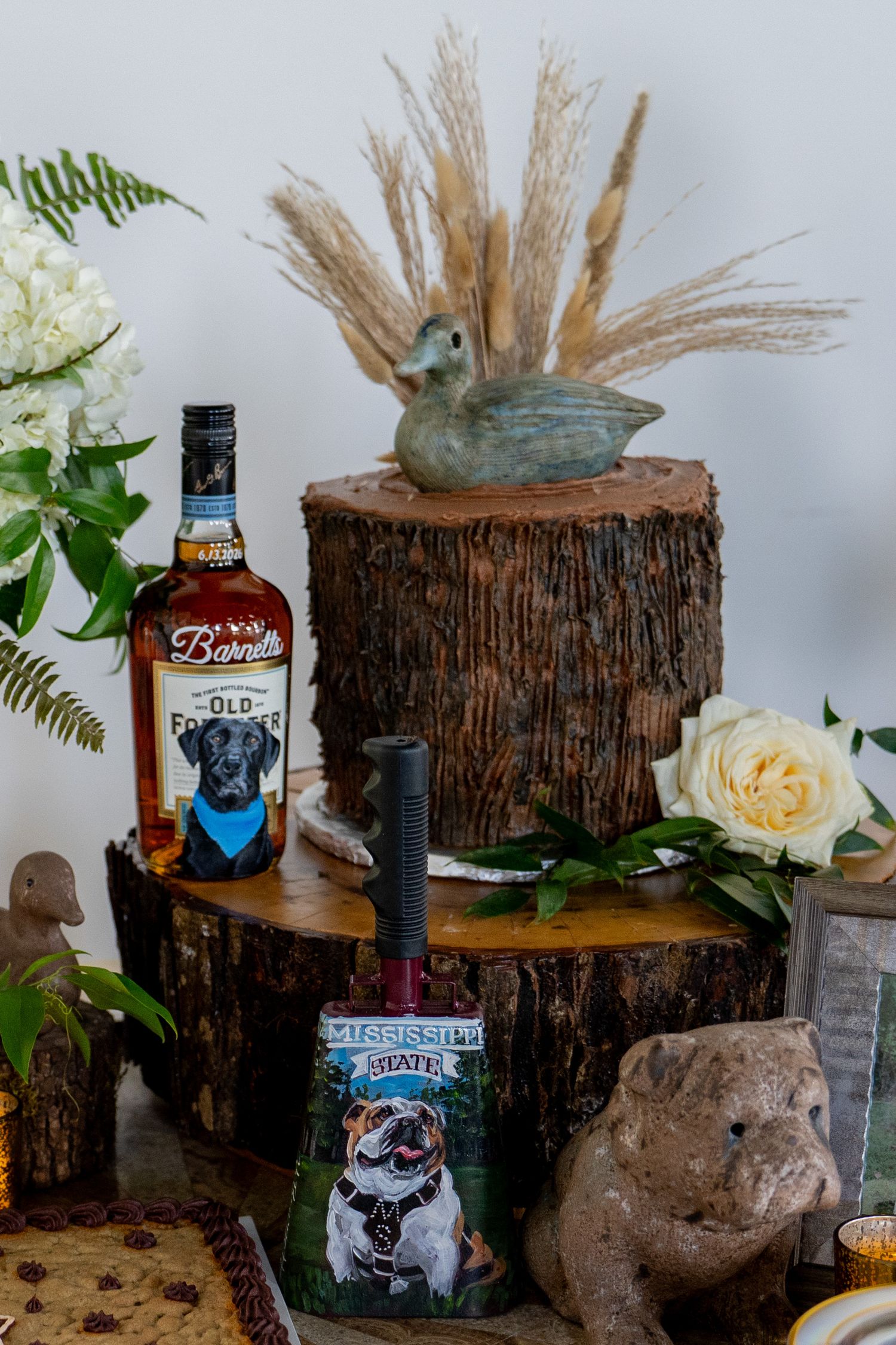 Rustic wedding decor with Barndt whiskey bottle, duck decoy on wood stump, white roses, and Mississippi State sign.