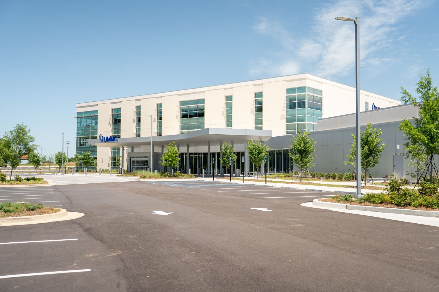 Modern commercial building with glass facade, spacious parking lot, and landscaped surroundings on a sunny day.