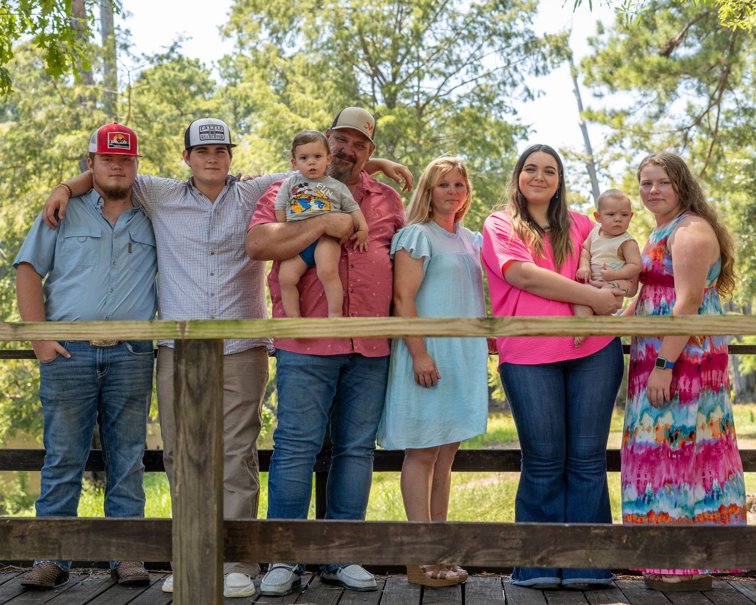 Family group photo on a wooden bridge outdoors, smiling together surrounded by lush green trees.
