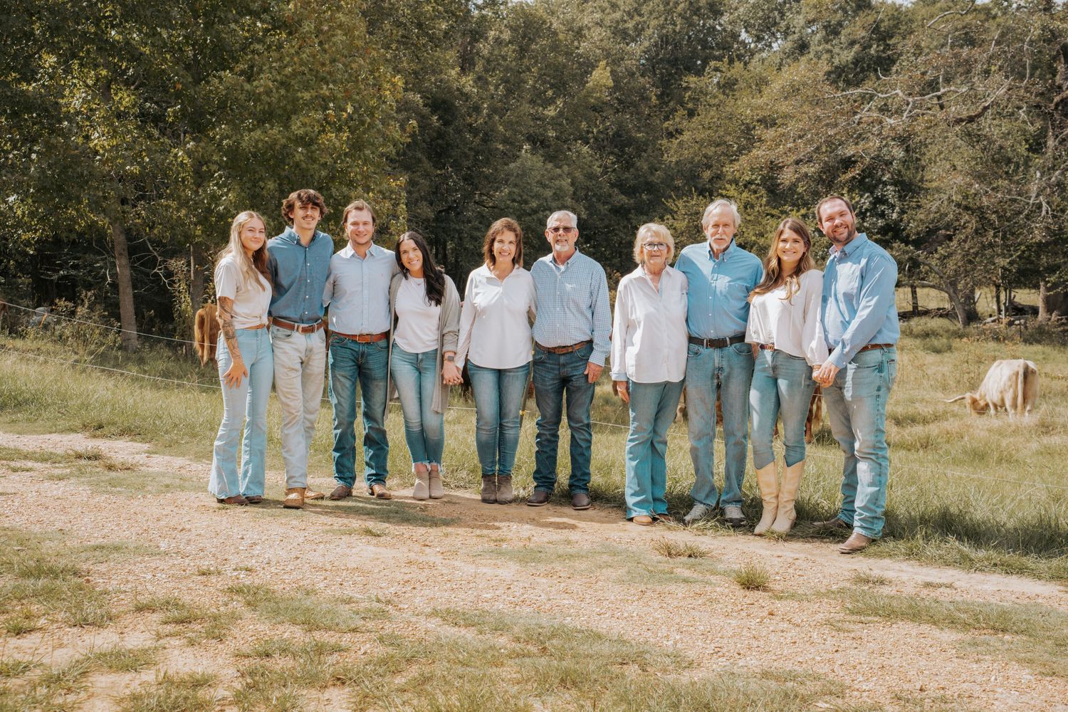 A large family group poses together outdoors on a gravel path surrounded by green fields and trees.
