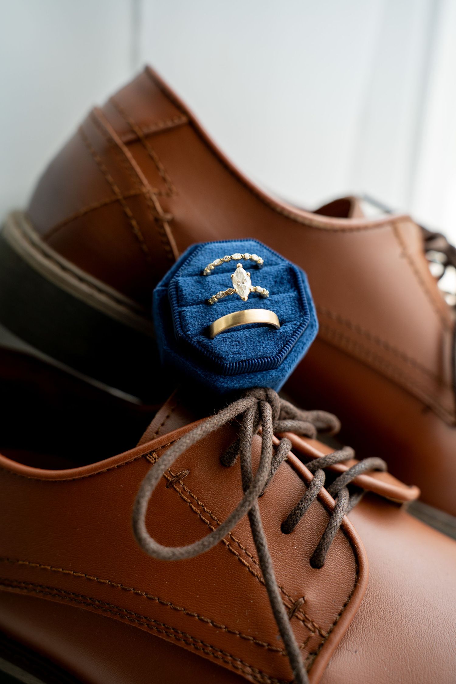 Gold wedding rings displayed in a blue velvet box resting on brown leather lace-up dress shoes.
