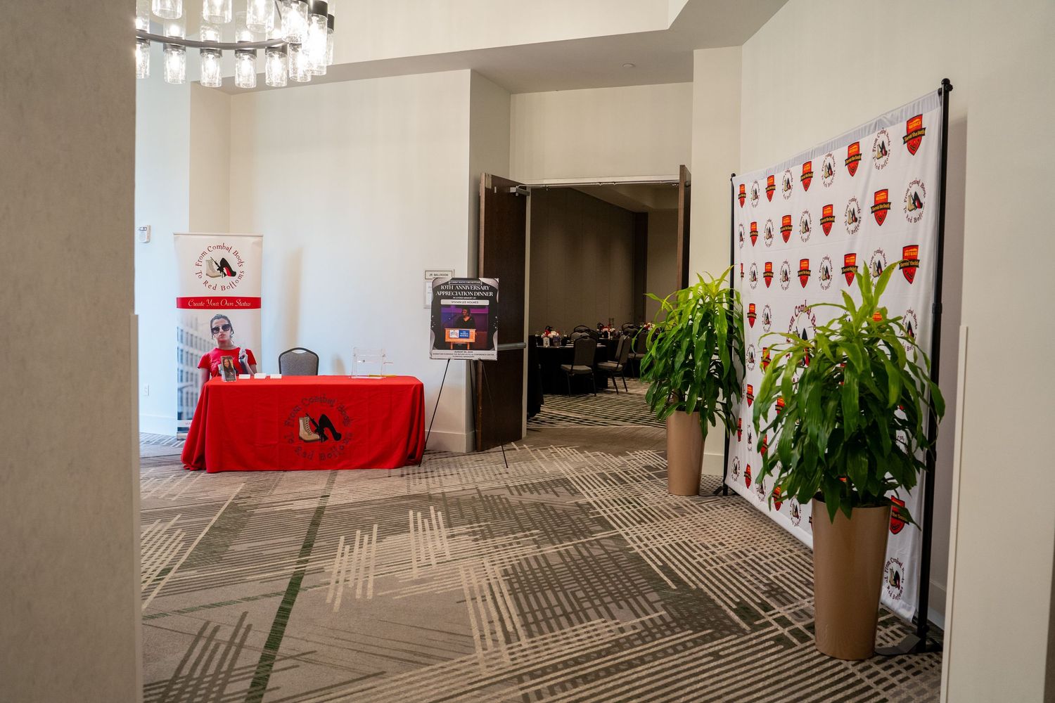 Conference registration desk with red tablecloth, step-and-repeat banner, and green plants in a hotel ballroom foyer.