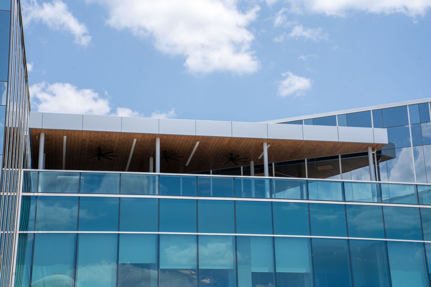 Modern glass office building exterior reflecting blue sky and clouds on a sunny day.