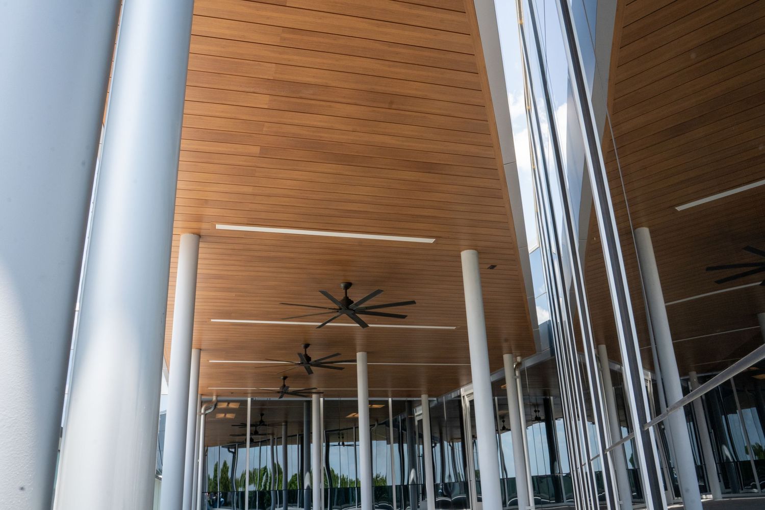 Modern covered patio with wood ceiling, black ceiling fan, and sleek metal columns in contemporary architecture.