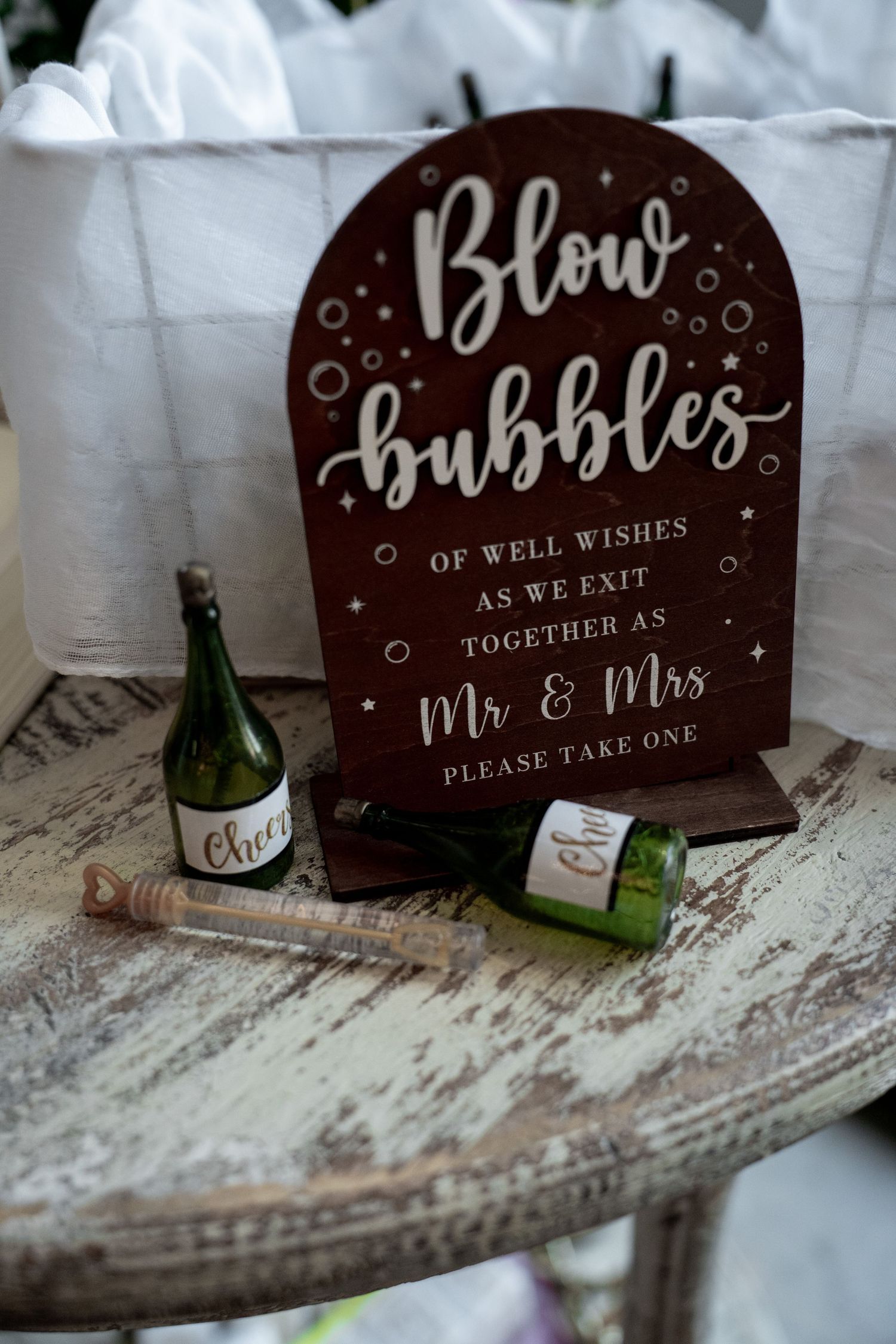 Wedding bubble wands in champagne bottle holders beside a rustic wooden Blow Bubbles Mr & Mrs sign on a vintage table.