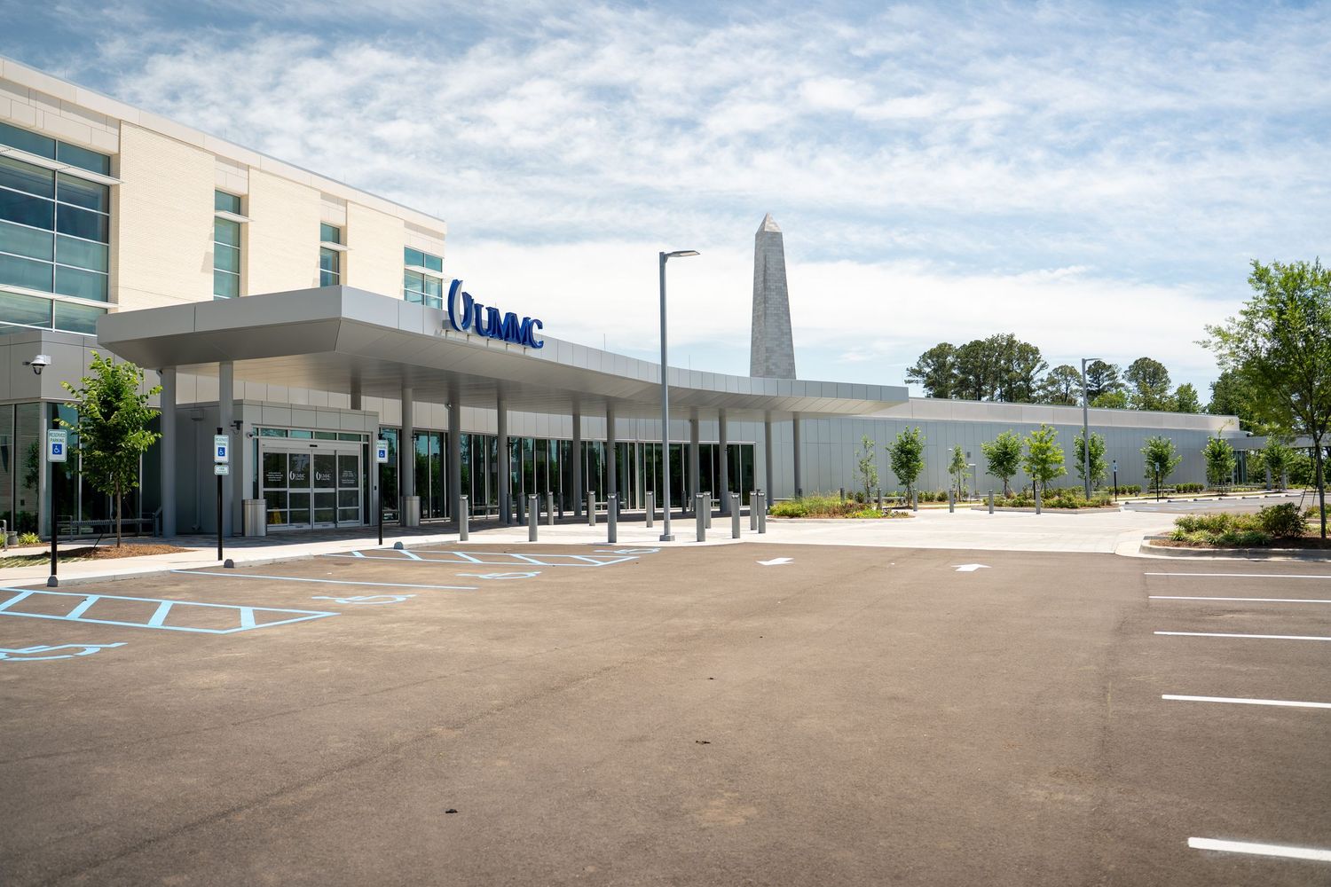 Modern UPMC medical facility exterior with spacious parking lot, glass entrance, and tall monument sign under cloudy sky.