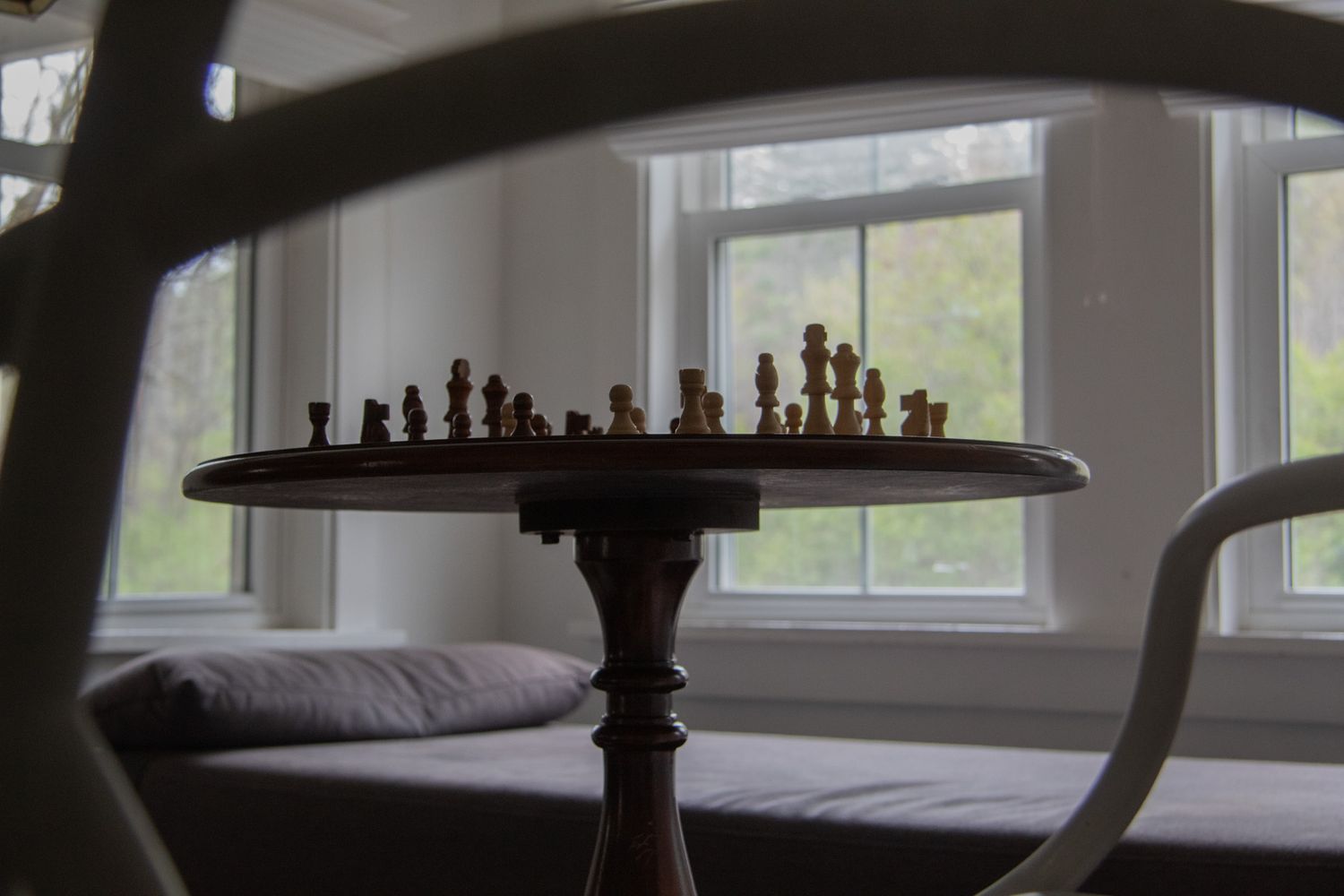 Wooden chess set displayed on a round pedestal table near a bright window in a cozy room.