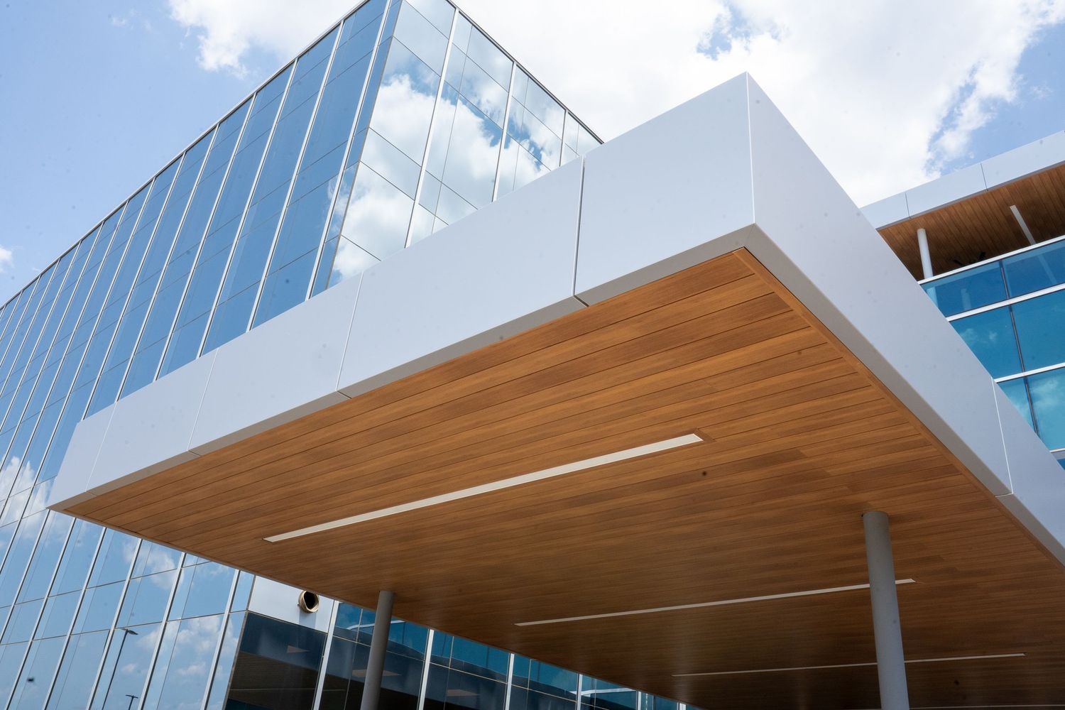Modern glass building exterior with wooden ceiling canopy under blue sky.