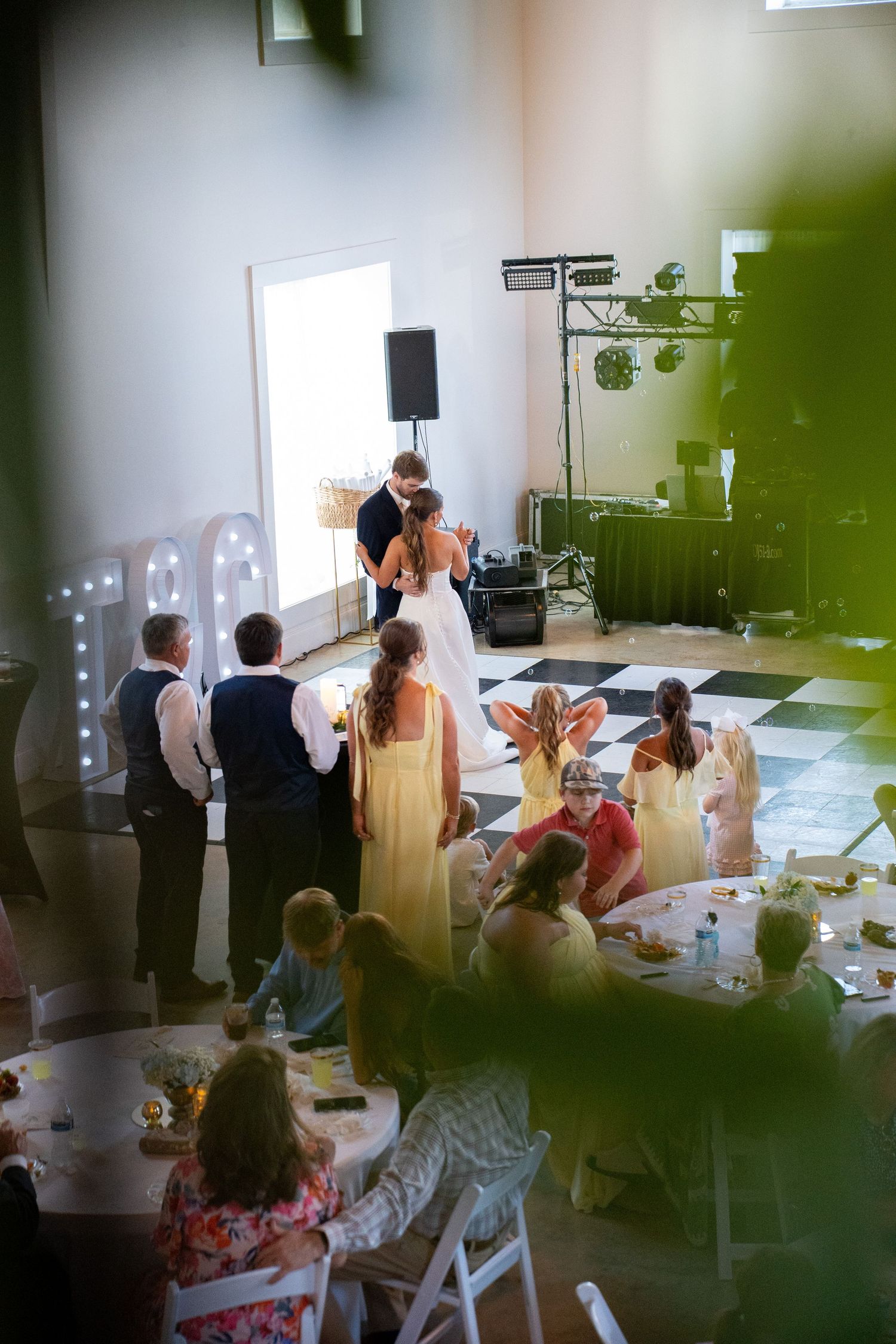 Bride and groom share first dance at wedding reception while guests sit at round tables in elegant venue.