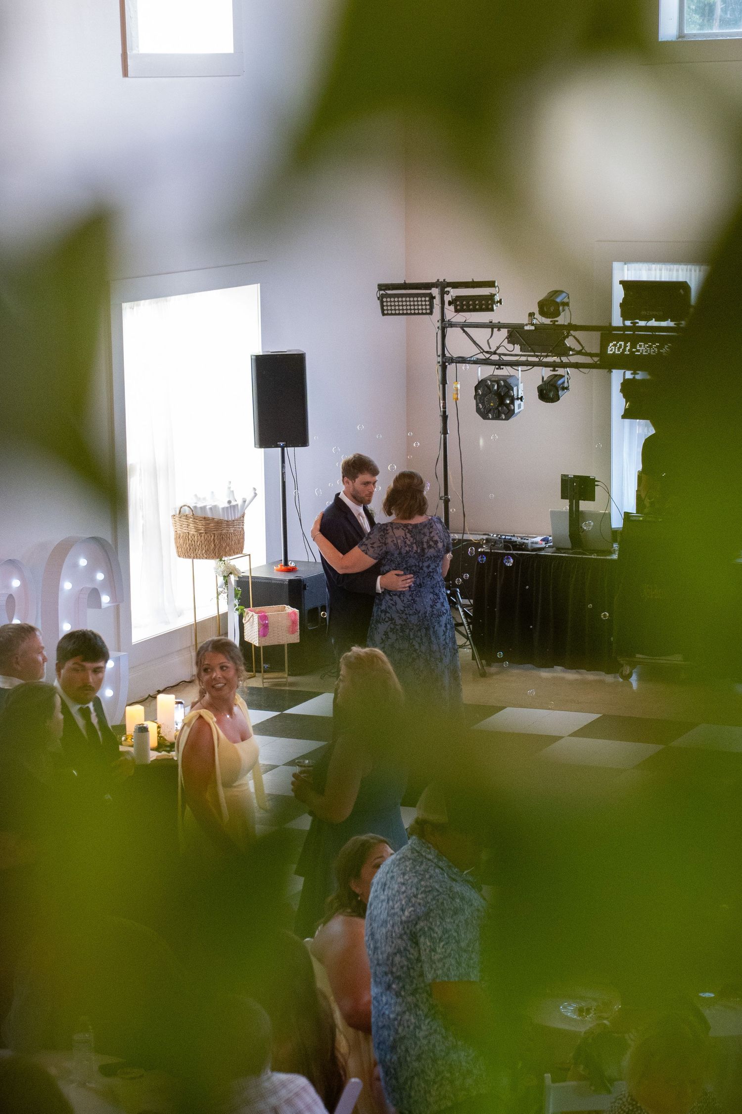 Couple sharing a first dance at a wedding reception with DJ equipment and checkered floor in background.