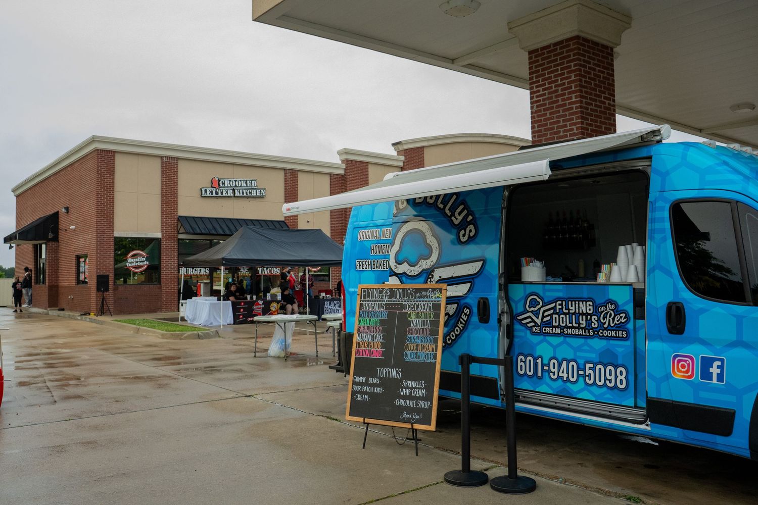 Blue food truck with phone number 601-940-5098 parked outside a brick strip mall on a rainy day.