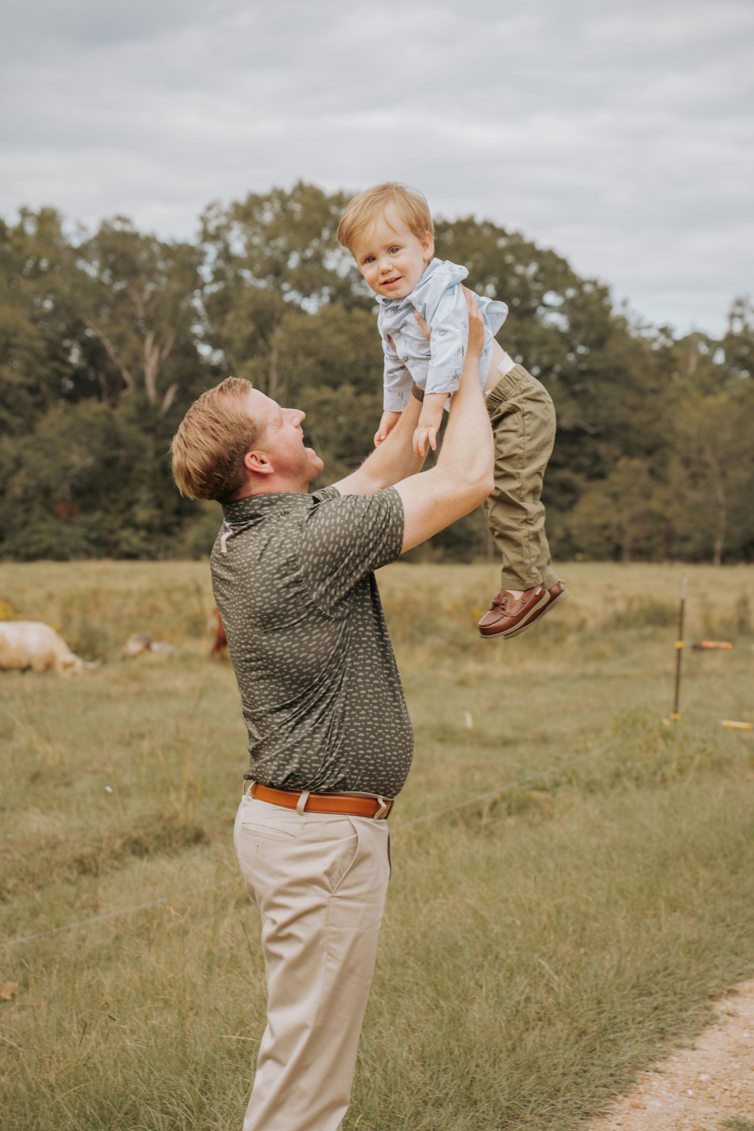 Father joyfully lifting toddler son high in the air in a green field, sharing a happy outdoor moment.