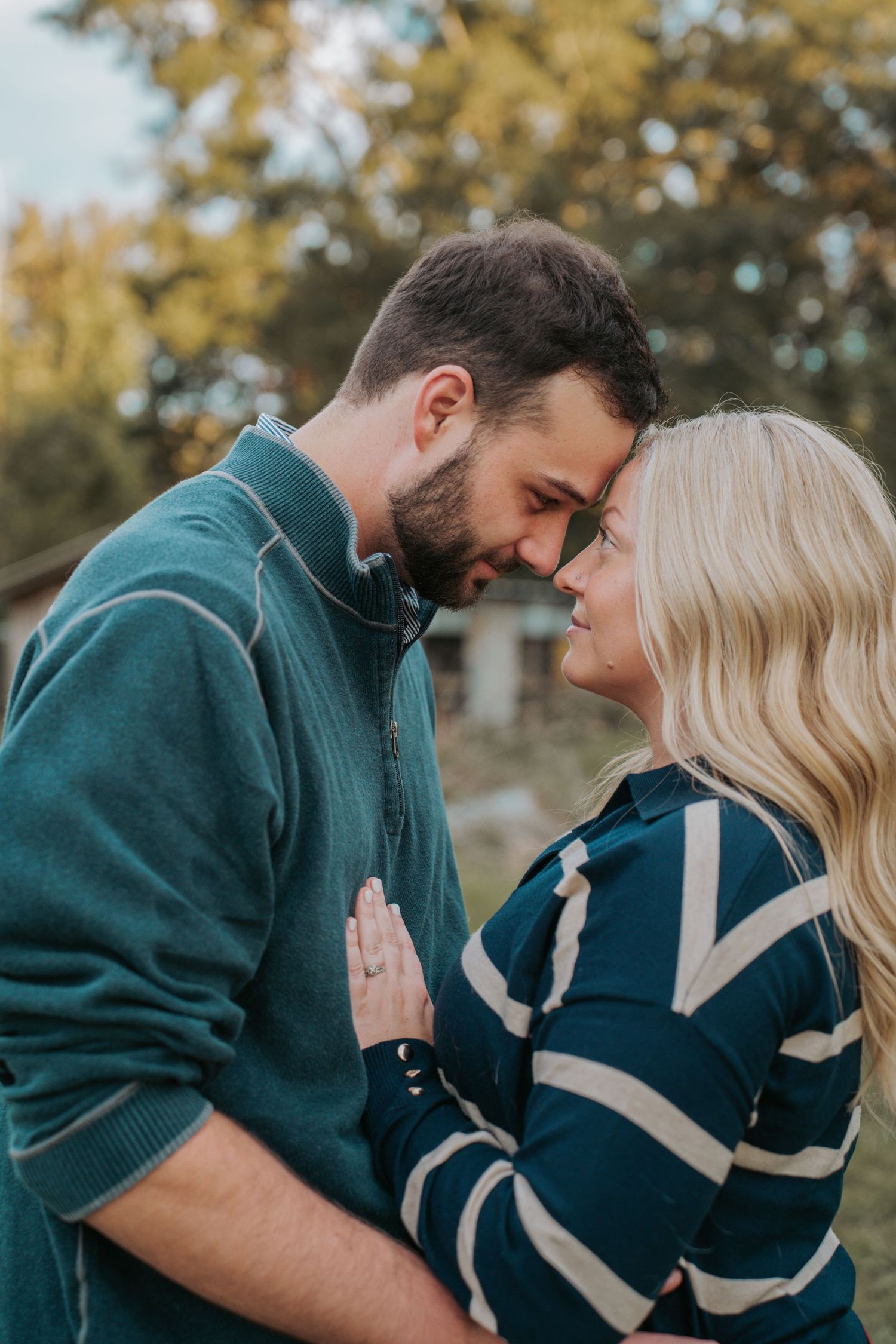 A couple shares a romantic forehead-to-forehead moment outdoors in autumn, wearing casual blue outfits.