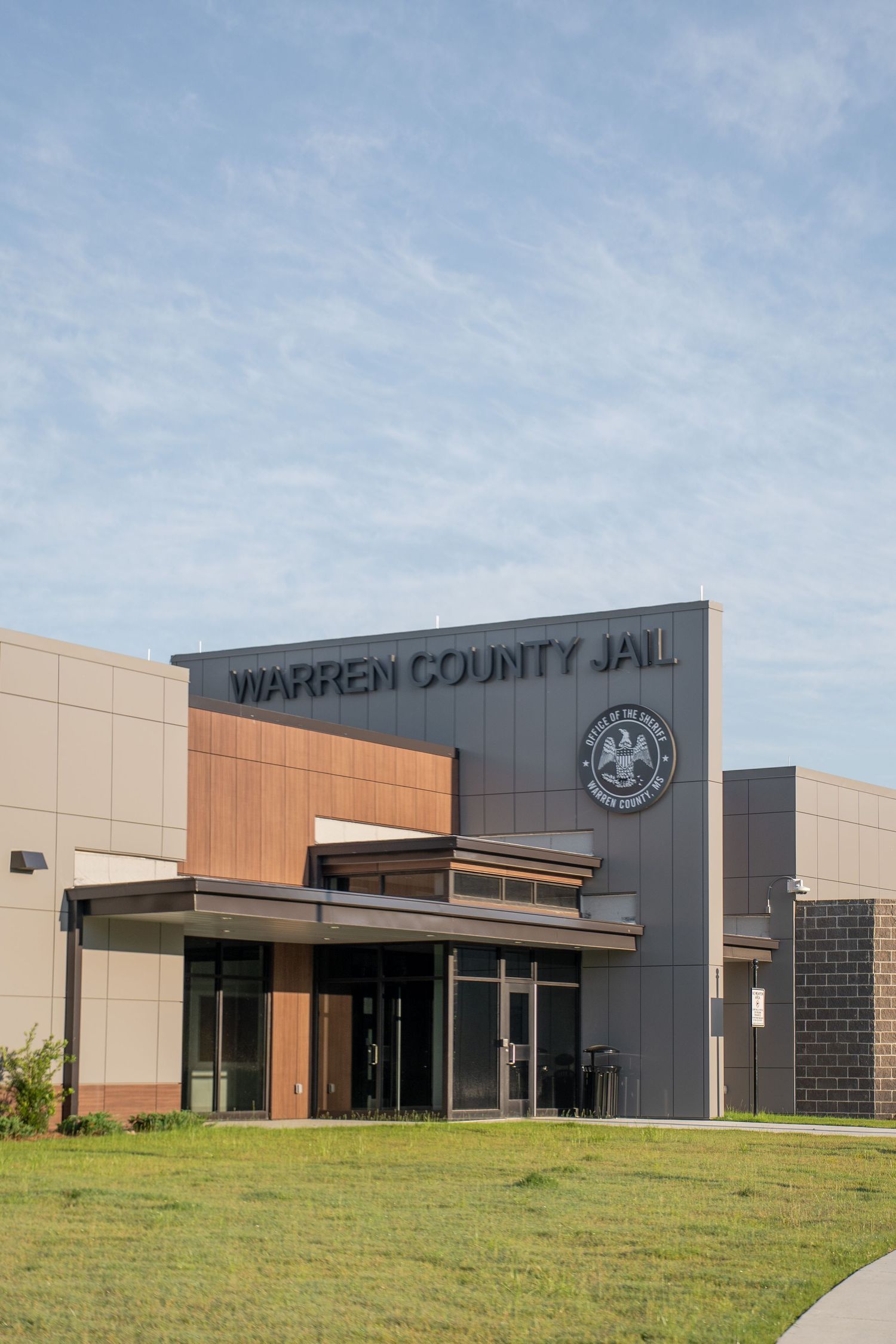 Exterior view of Warren County Jail building with modern architecture, county seal, and manicured lawn under blue sky.