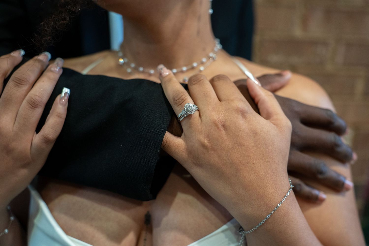 Close-up of a bride wearing diamond jewelry, necklace, ring, and bracelet, as hands adjust her wedding dress.