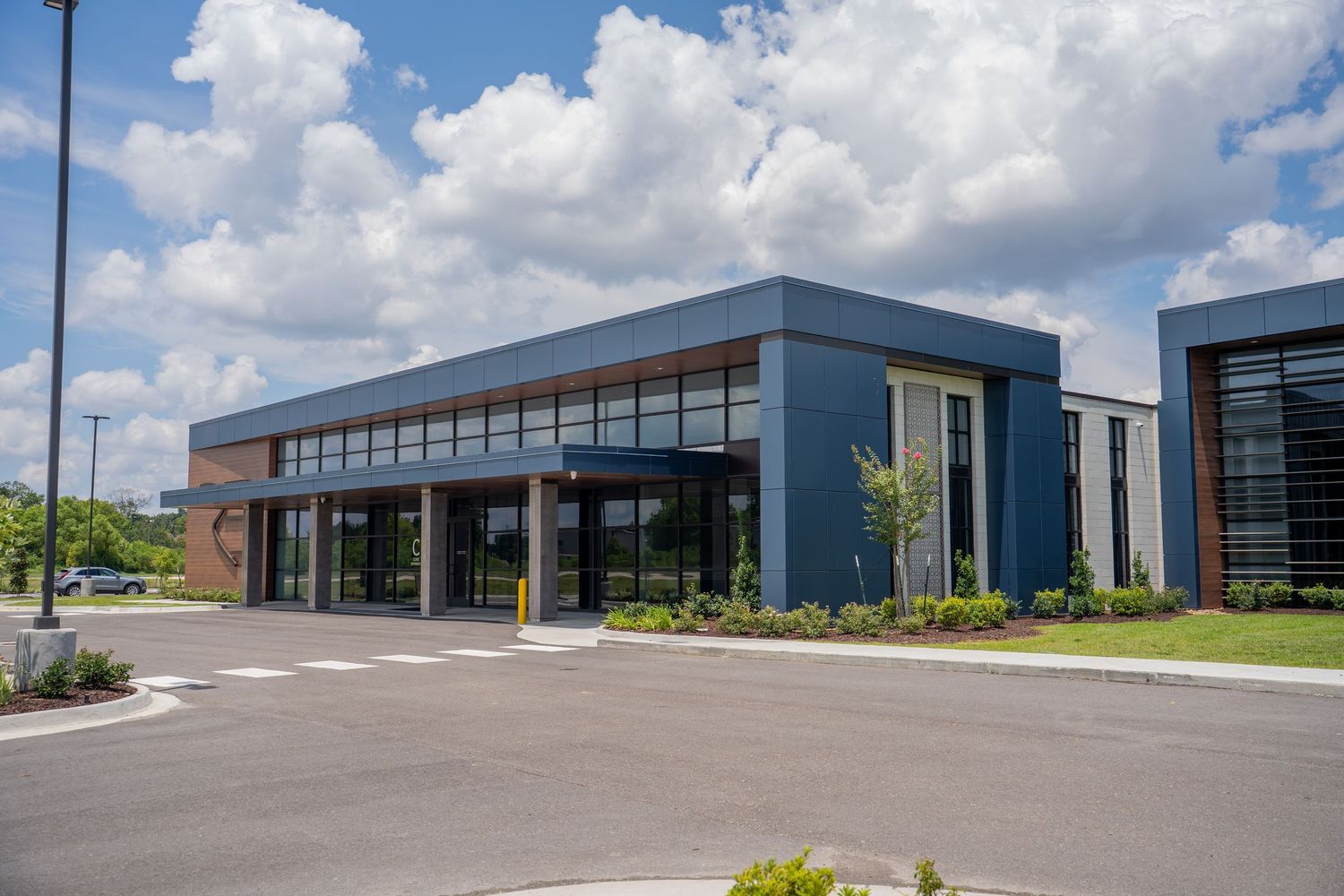 Modern commercial building with blue facade, large windows, and landscaped entrance under a partly cloudy sky.