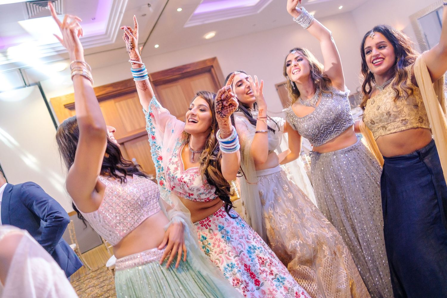 Festive indoor celebration with guests in formal attire dancing under purple lighting at an elegant venue.