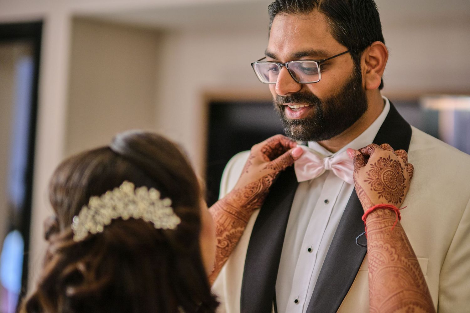 A couple shares a tender moment during their wedding preparations with intricate henna designs visible on hands.