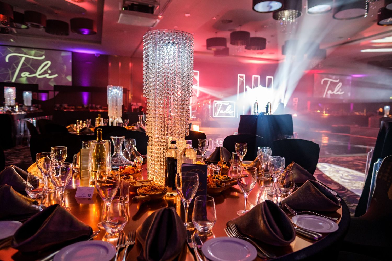 Elegant table setting with crystal chandelier centerpiece and ambient red lighting.