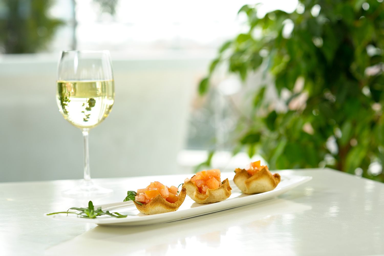 Two wine glasses and a white plate with appetizers sit on an elegant white tablecloth in a bright restaurant setting.