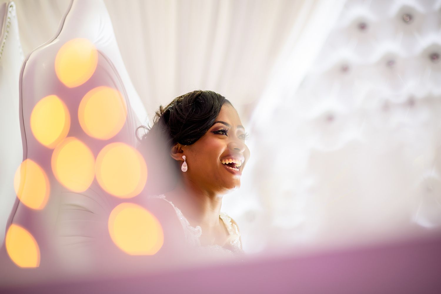 A side view of someone laughing with blurred golden bokeh lights in the background.