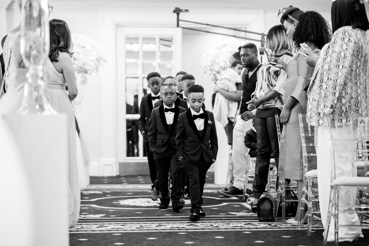 Wedding party members walking in procession outside traditional white building.