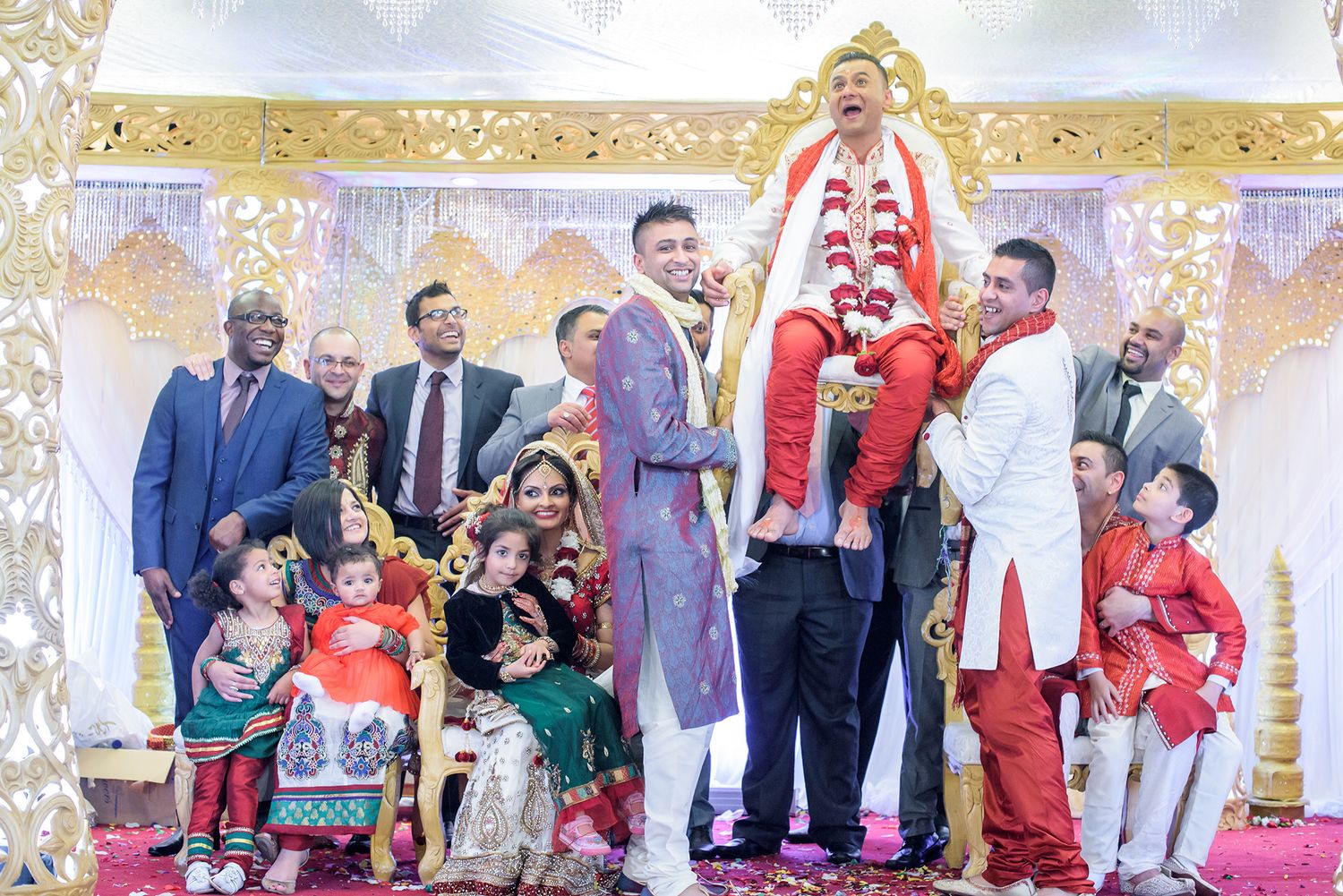 Wedding party and guests gathered for celebration with ornate gold backdrop decorations.