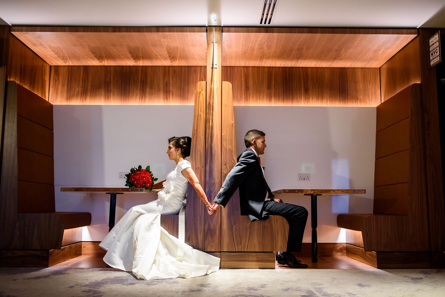 Wedding couple in elegant pose inside wood-paneled room with dramatic lighting.