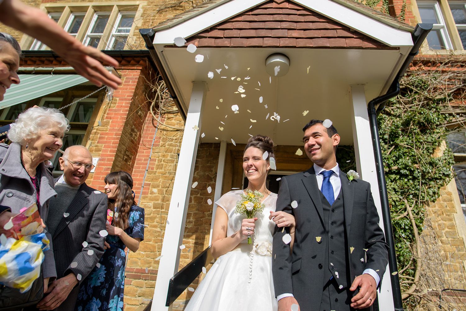 Wedding guests throwing confetti outside a brick building entrance.