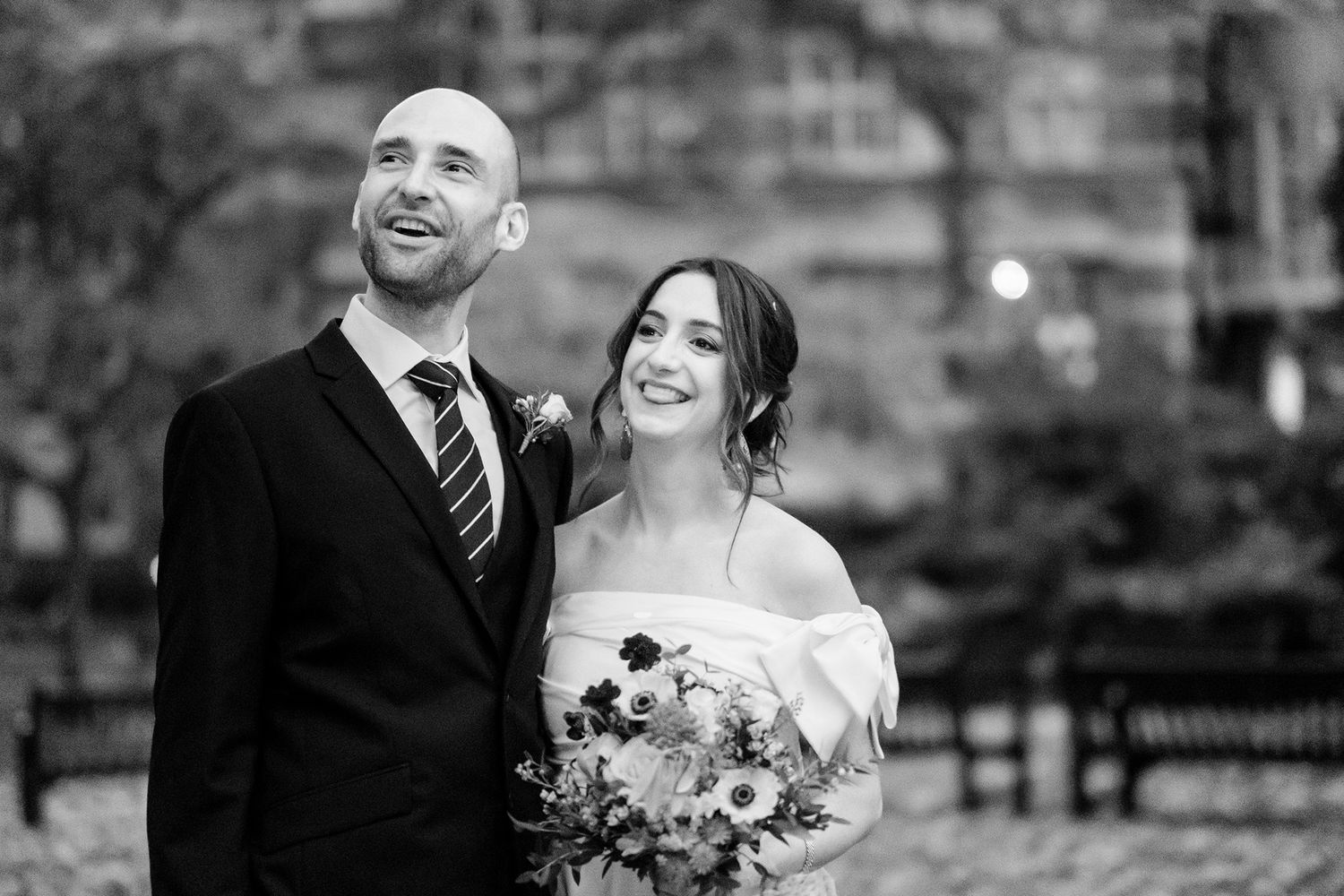 Elegant black and white wedding portrait capturing a joyful moment between newlyweds in front of stone architecture.