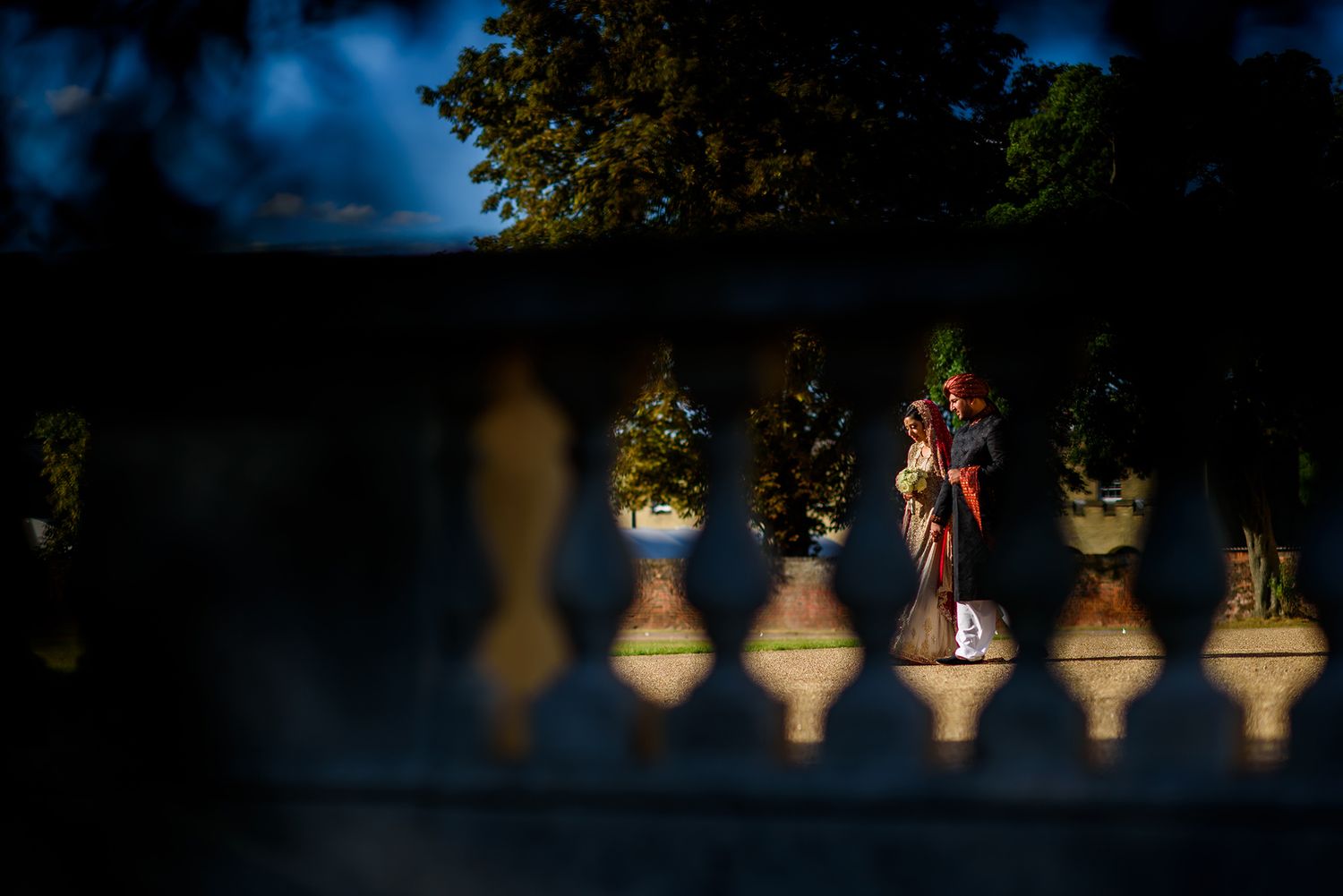 Artistic nighttime wedding photo through decorative balustrade with illuminated couple.