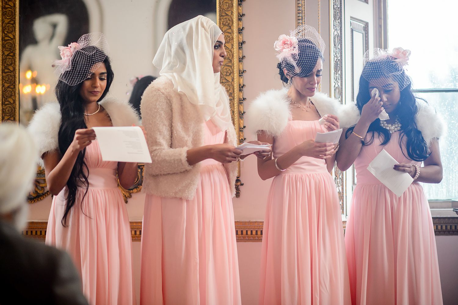 Bridesmaids in pink dresses preparing for the wedding in an ornate room with gilded mirrors.