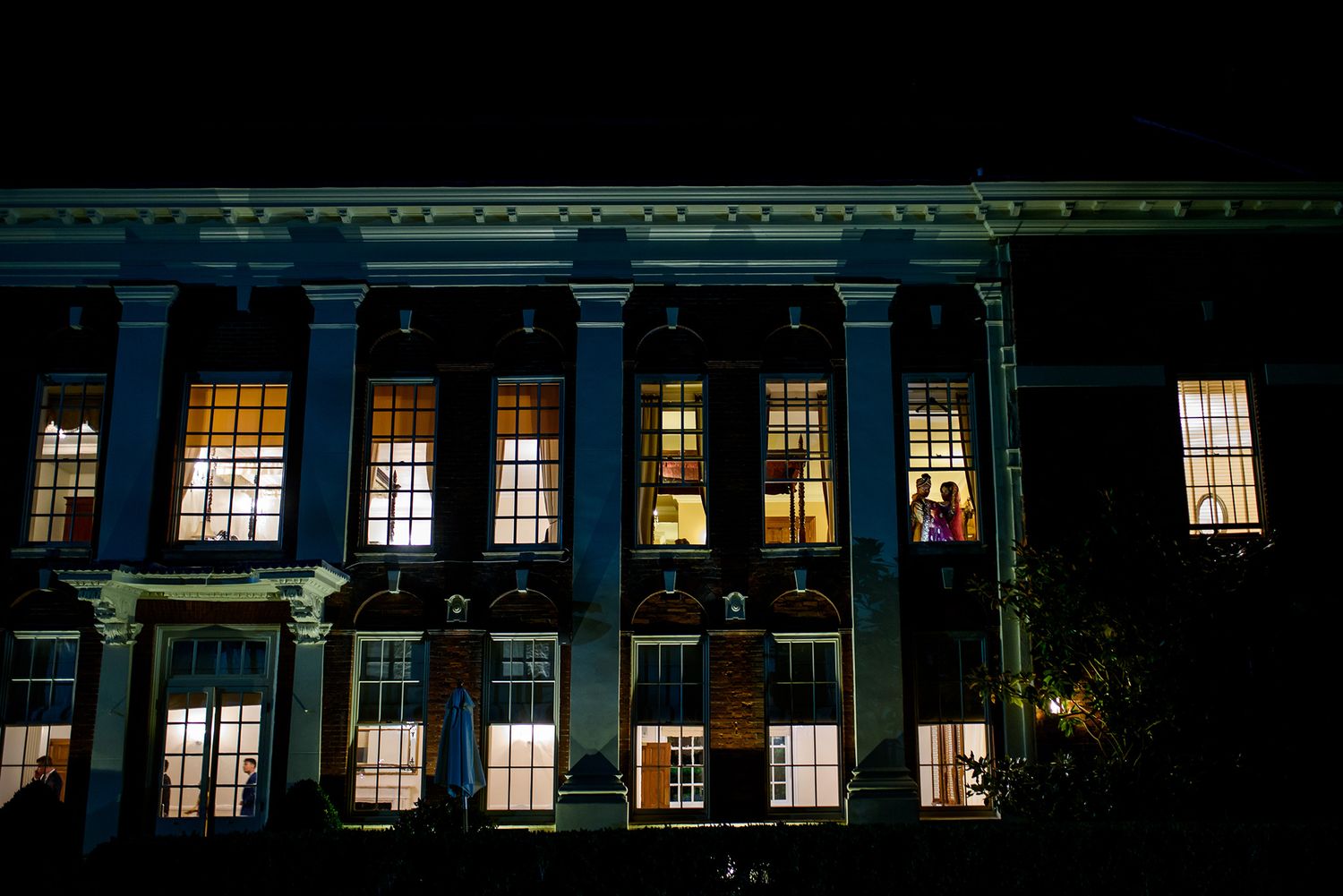 Night view of an illuminated building with glowing windows and neoclassical architecture.