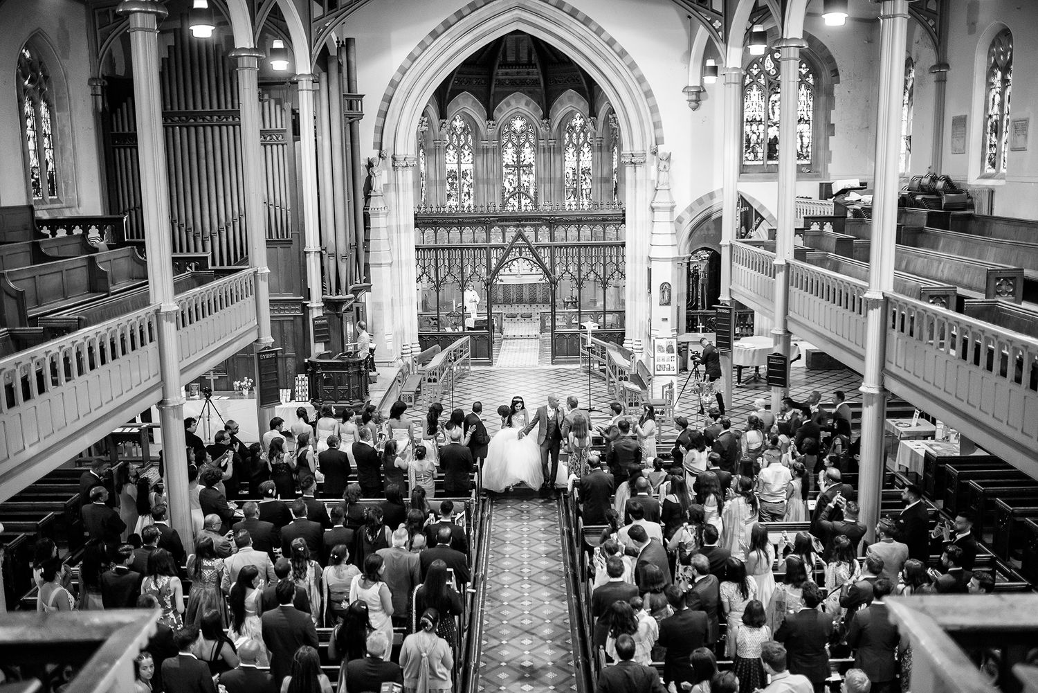Black and white panoramic view of wedding guests in historic church interior.