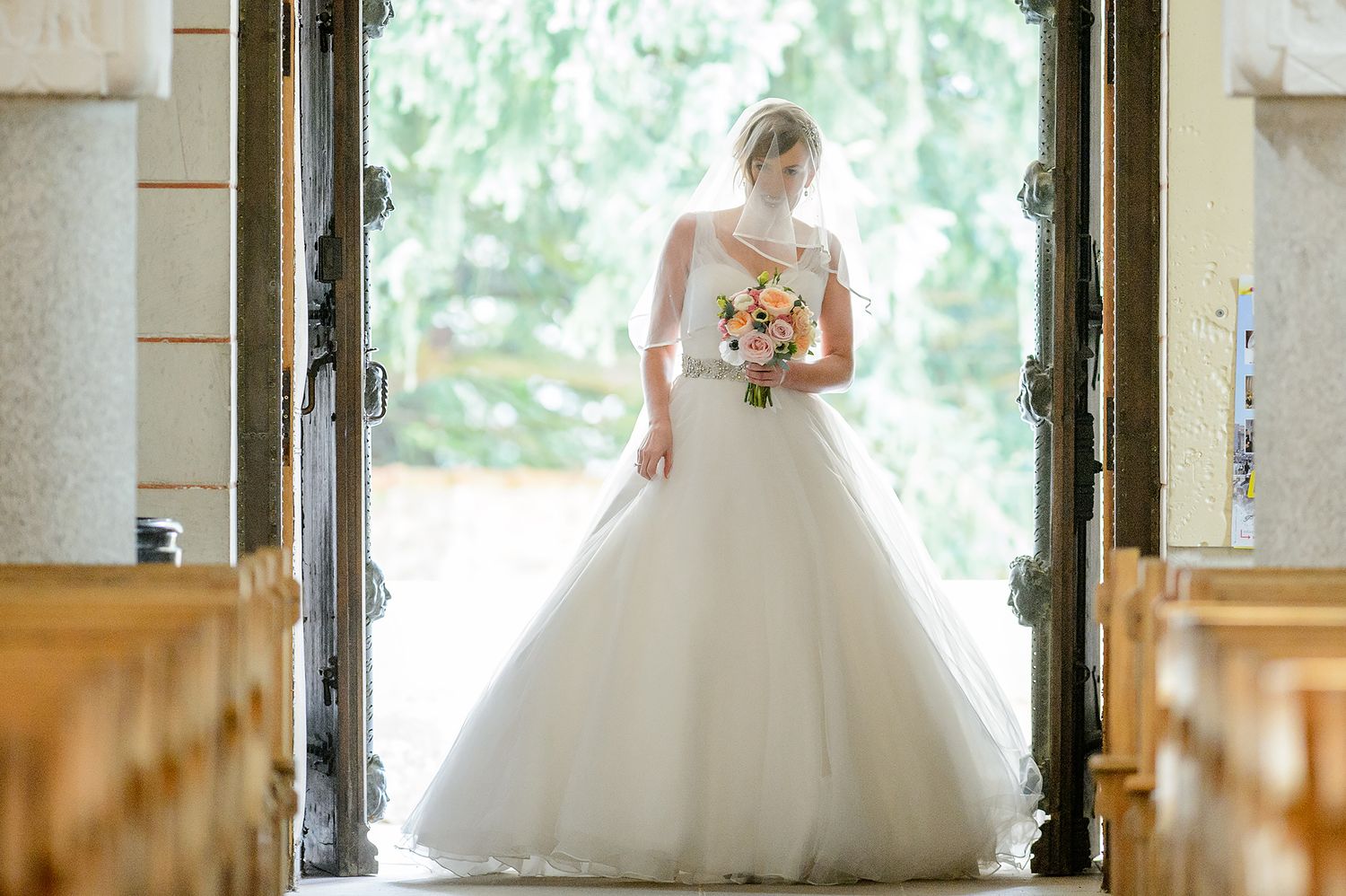 White wedding dress framed by elegant stone columns and natural outdoor lighting.