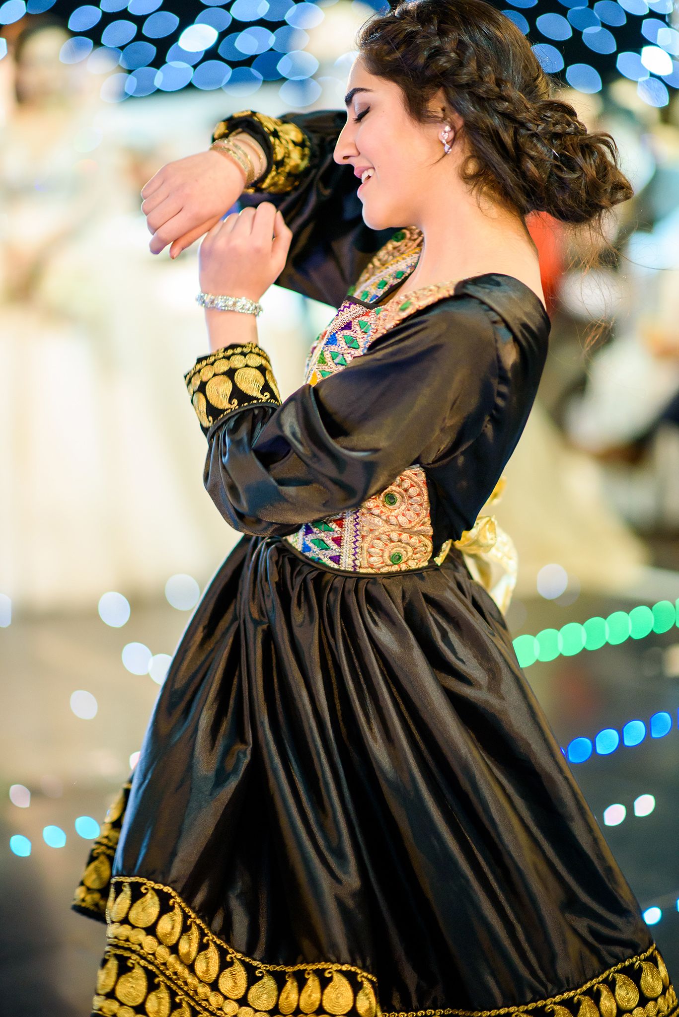 A performer spins in a traditional black dress with gold trim during a choreographed dance routine.