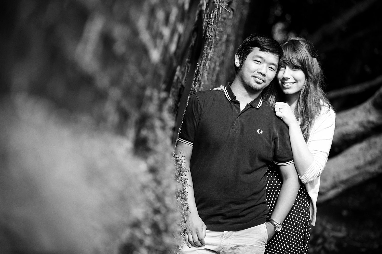An intimate black and white portrait of a couple against a blurred natural background.