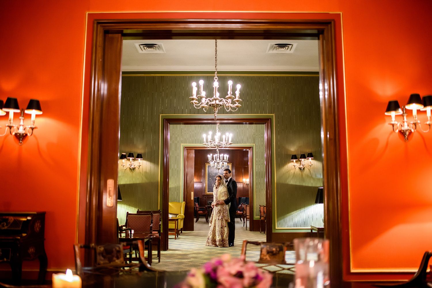 Elegant ballroom venue with red walls, ornate chandeliers and wall sconces creating a warm ambiance.